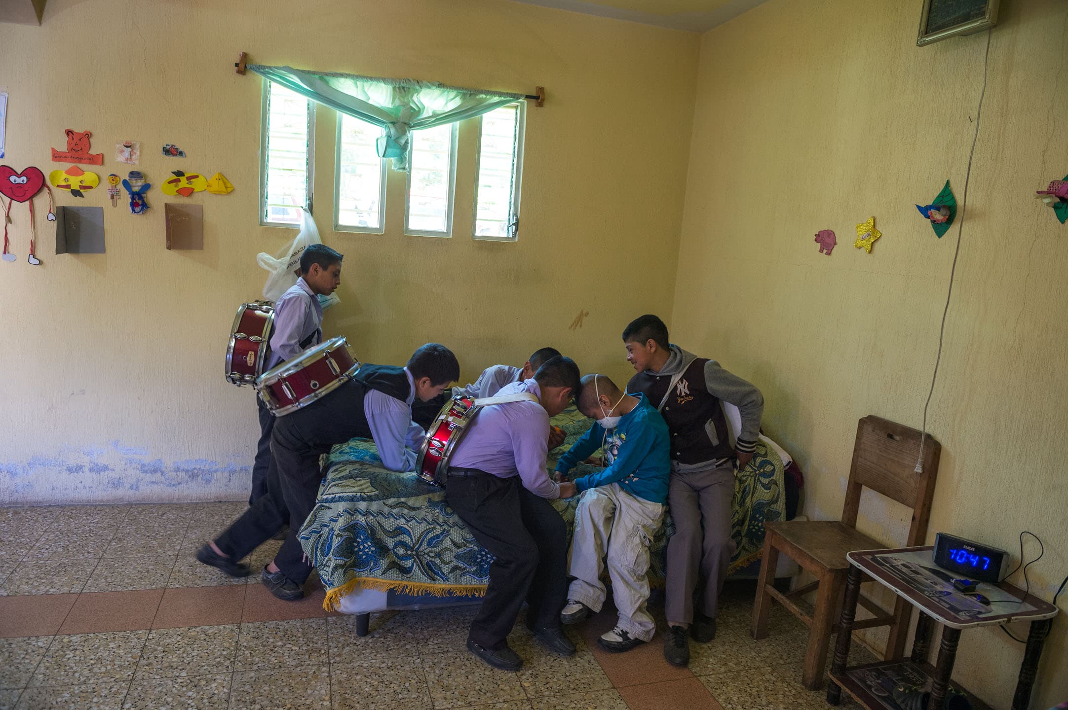 Heber Menchu Tamayac, 8, sits on the bed inside his family’s shared bedroom in San Cristobal, Totonicapan, Guatemala, while his friends console him.