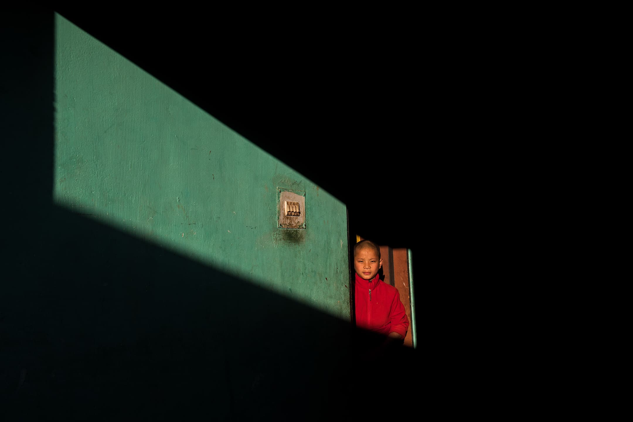A young novice monk stands in a slice of golden hour light at Chimi Lhakhang, a Buddhist monastery perched on a hill just outside Punakha, Bhutan on December 6, 2017.  Bhutan’s natural light is soft and golden and while smiling monks in flowing maroon robes inhabit the ancient monasteries that dot the craggy countryside.  The young boy posed for this portrait at the request of the photographer.