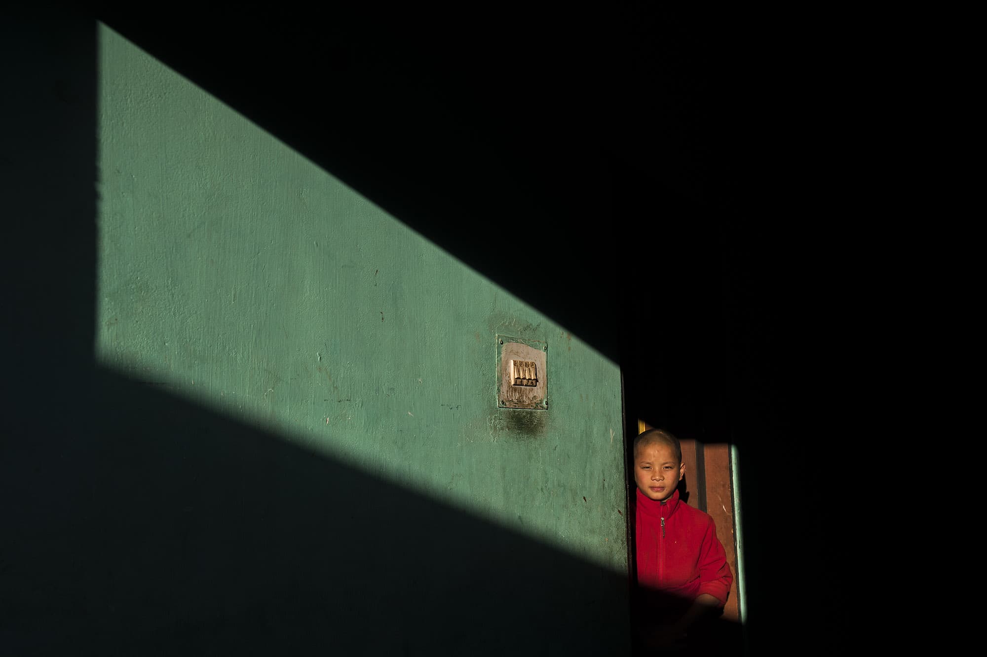 A young novice monk stands in a slice of golden hour light at Chimi Lhakhang, a Buddhist monastery perched on a hill just outside Punakha, Bhutan on December 6, 2017.  Bhutan’s natural light is soft and golden and while smiling monks in flowing maroon robes inhabit the ancient monasteries that dot the craggy countryside.  The young boy posed for this portrait at the request of the photographer.